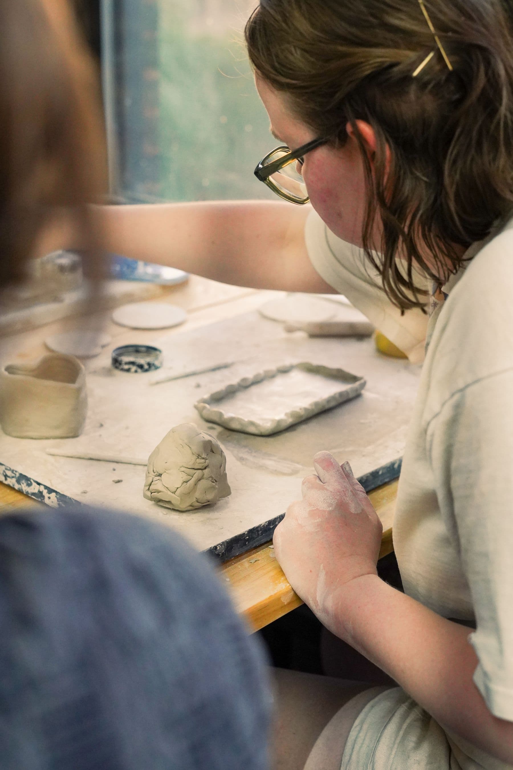 A guest leaning over the worktable, hands in clay, entirely absorbed