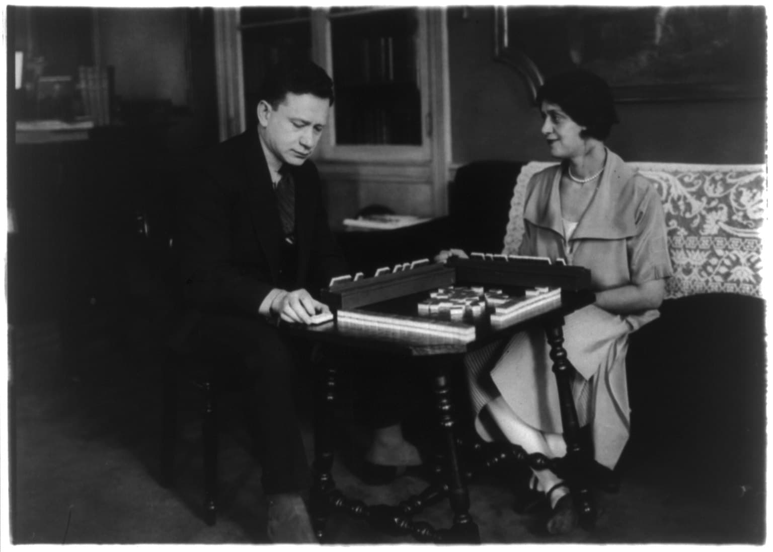 Black and white photograph of a husband and wife sitting across from each other at home, playing mahjong