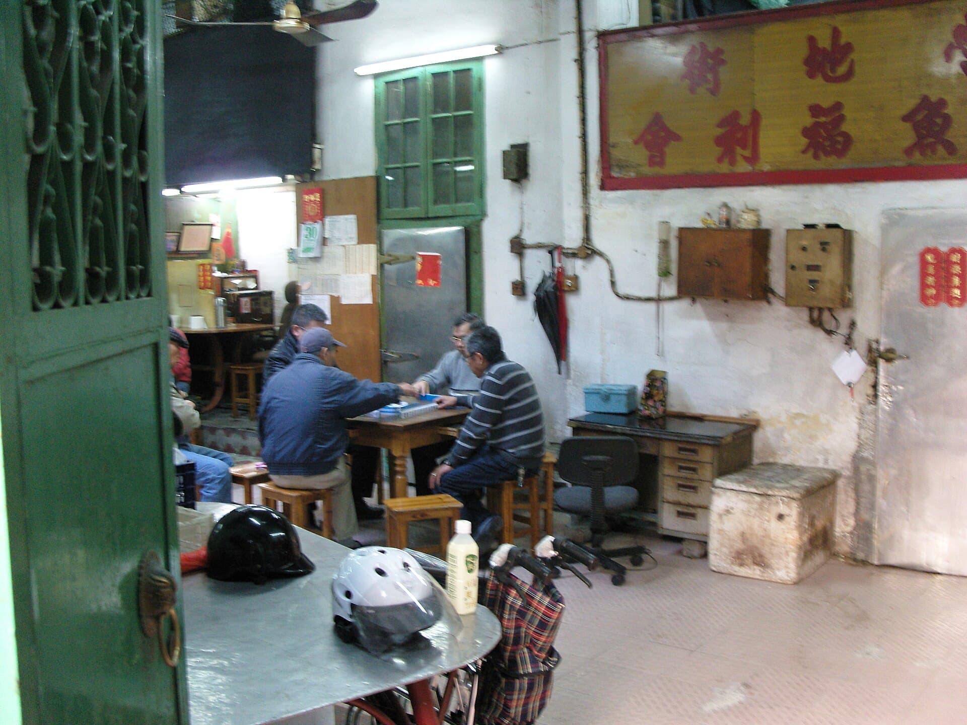 Photograph of four men playing mahjong in a room beside a temple