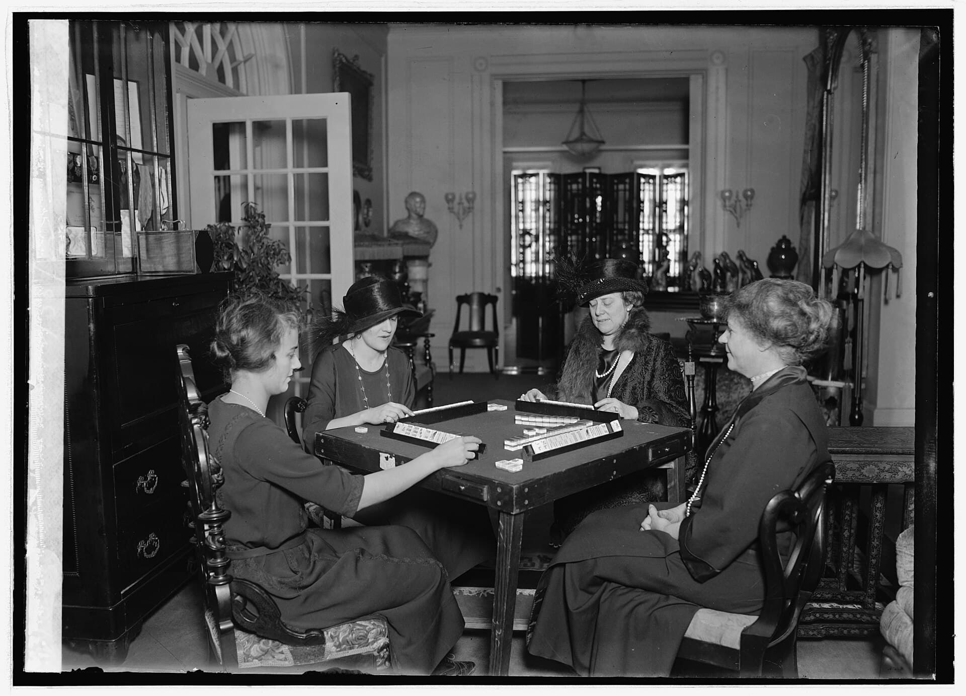 Black and white photograph of four women in a parlor playing mahjong at a card table