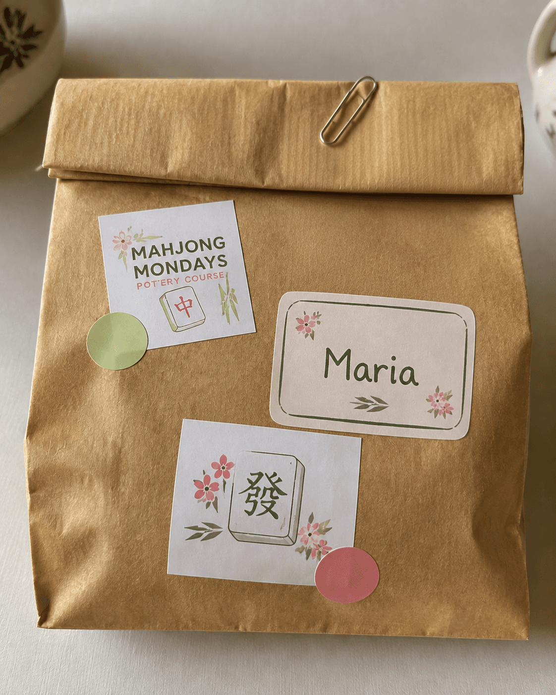 Kraft paper takeaway bag with a Mahjong Mondays sticker and a hand lettered name label