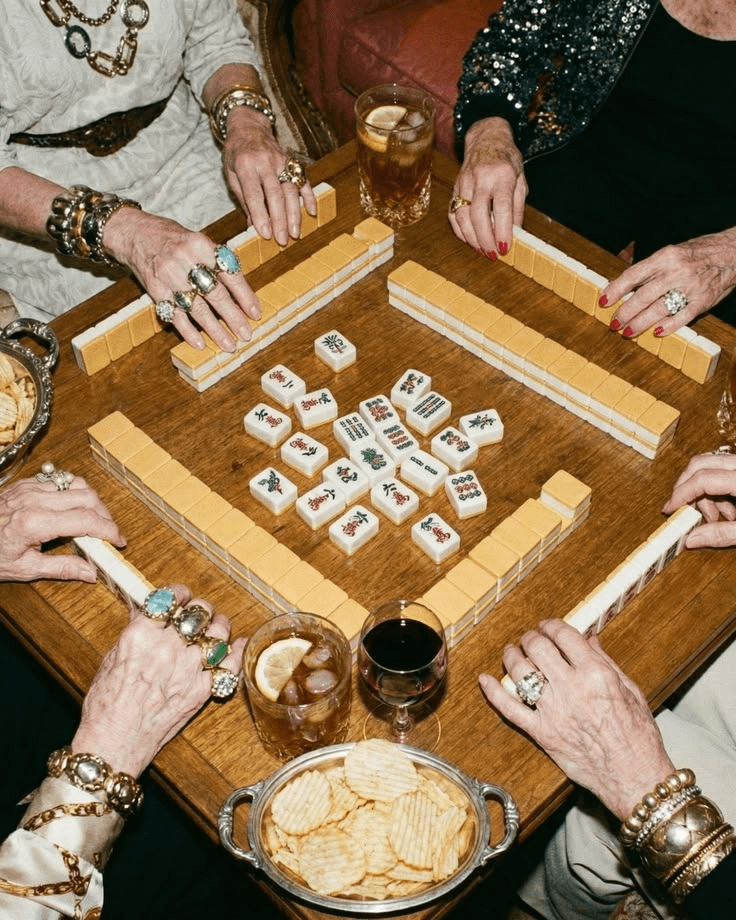 Overhead view of four players mid game around a mahjong table with tiles, racks, and drinks