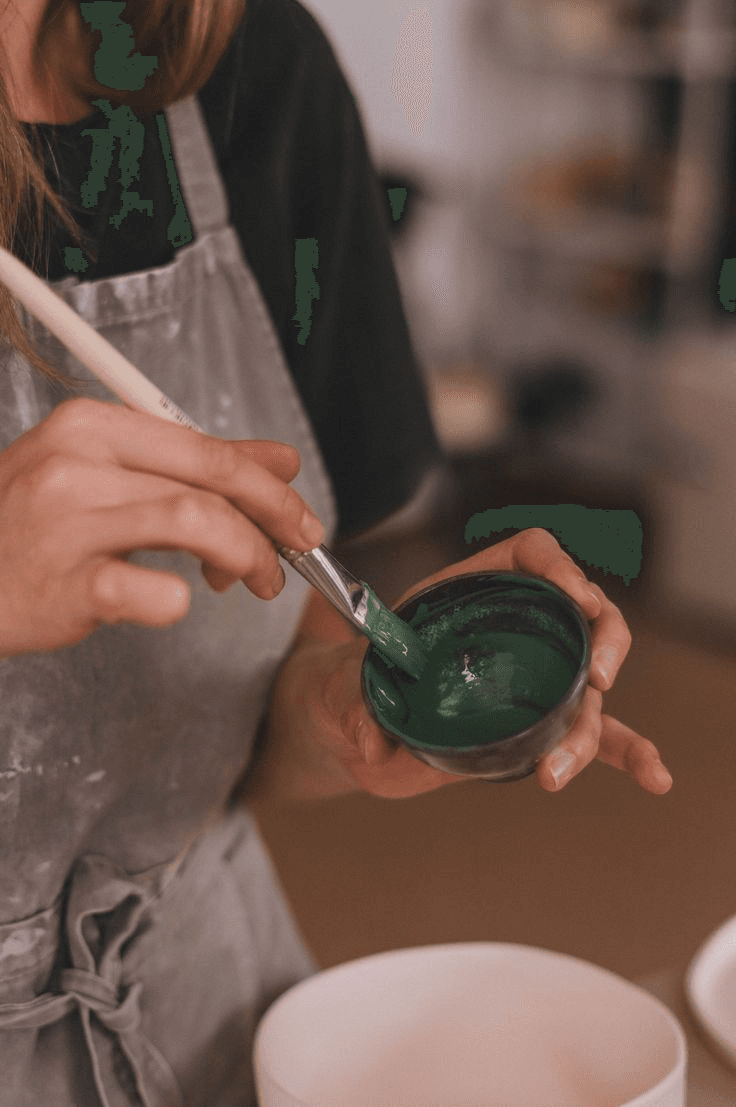 Student in a studio apron brushing green glaze onto a small ceramic bowl