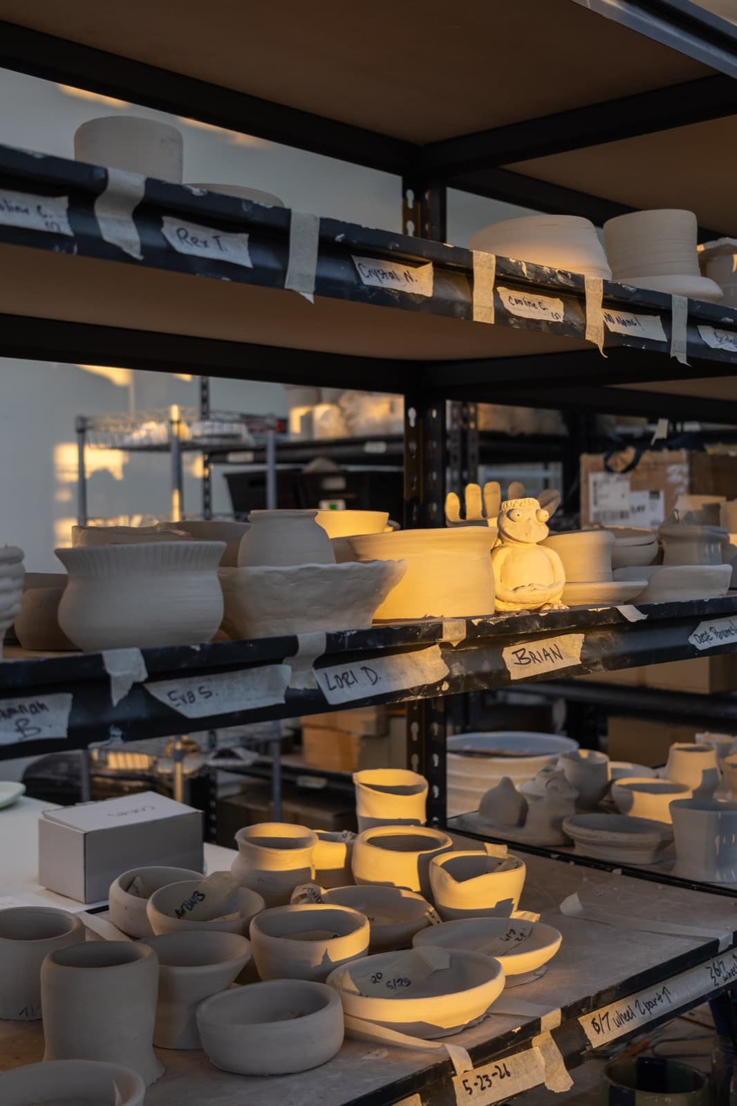 Shelves of finished pottery pieces, warmly lit