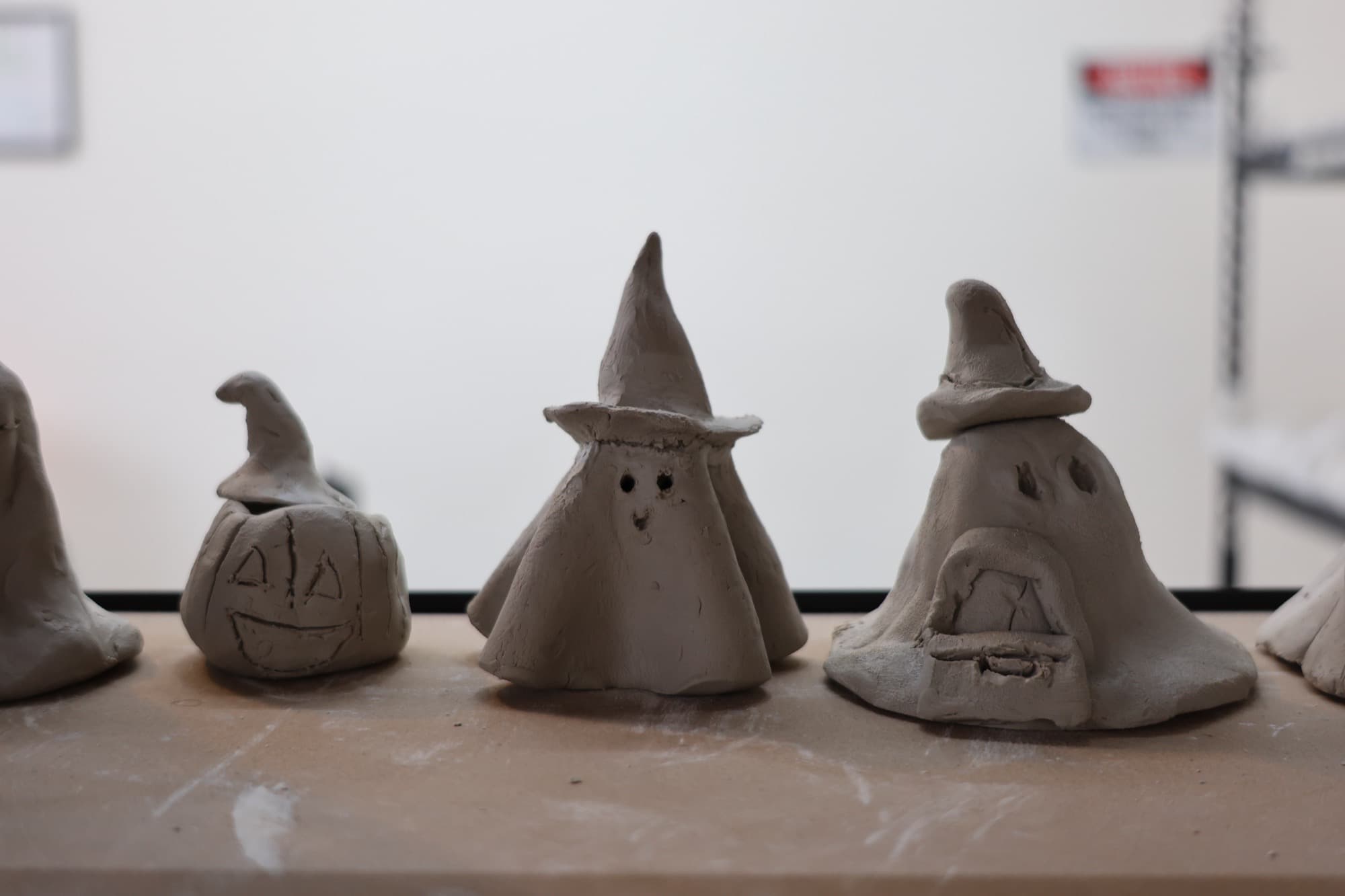 A row of handbuilt clay Halloween figures made by kids in our classes — a jack-o'-lantern, little ghosts, and witch hats