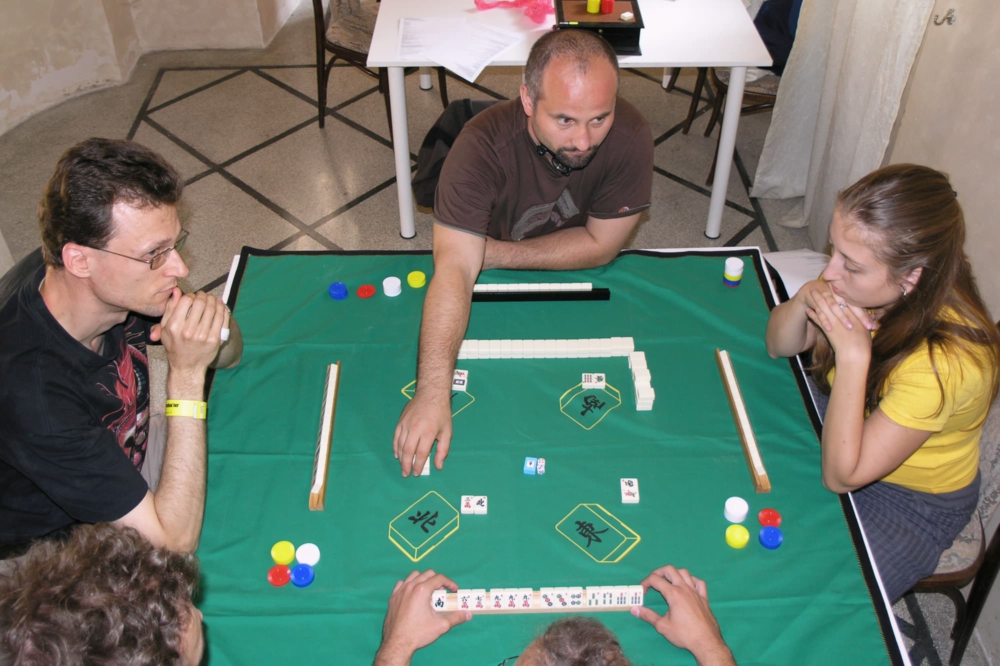 Friends leaning in over a traditional style mahjong game on a green felt table at a board game festival